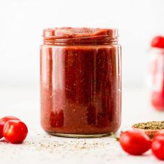 a jar filled with red sauce next to tomatoes and seasoning on the counter top