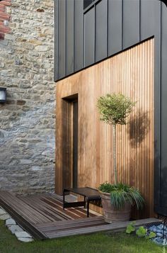 a small tree in a pot next to a wooden bench on the grass near a building