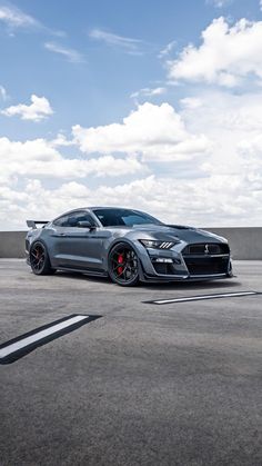 a gray sports car parked in an empty parking lot under a blue sky with clouds