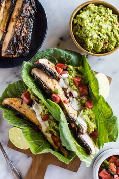 fish and guacamole are served on lettuce leaves with lime wedges