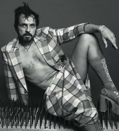 a shirtless man sitting on top of a pile of spikes wearing shorts and socks