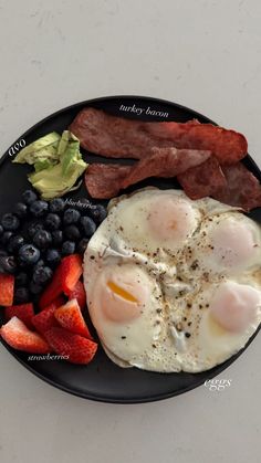 the plate has eggs, bacon, strawberries and blueberries on it