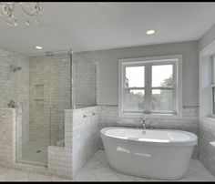 a white bath tub sitting under a window next to a sink and shower stall in a bathroom