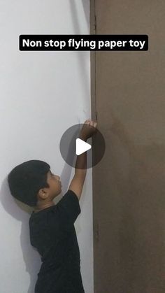 a young boy standing in front of a wall with a paper toy hanging from it's side