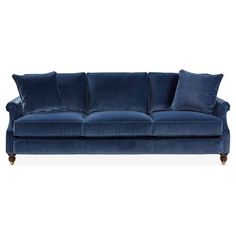 a blue velvet couch with pillows on the arm and back cushions, in front of a white background