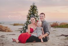 a man, woman and child sitting in front of a christmas tree on the beach