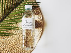 a bottle of water sitting on top of a straw hat next to a palm leaf