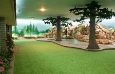 an indoor golf course with artificial grass and trees in the background, surrounded by fake rocks