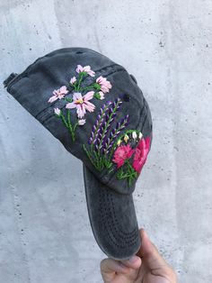 a person holding up a gray hat with flowers on the front and side of it