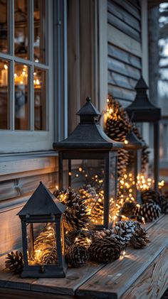 three lanterns with pine cones and lights on the porch