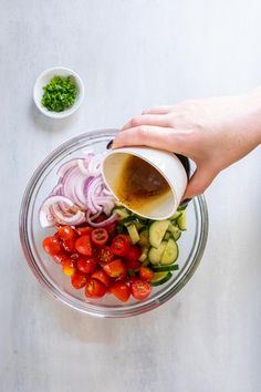 someone pouring dressing into a glass bowl filled with chopped vegetables and sauce on the side