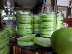 several jars filled with pickles sitting on top of a wooden table next to an apple