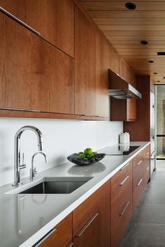 a modern kitchen with wood cabinets and stainless steel sink, along with an open glass door leading to the outside patio