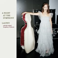 a woman in a white dress standing next to a red and white guitar case with the words, a night at the symphy laufy written on it