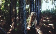 a woman standing next to a tree in the woods