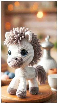 a small crocheted pony sitting on top of a wooden table next to a cup and saucer