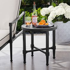 an outdoor table with two drinks and oranges on it next to a white chair