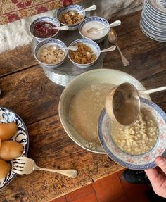 a person pouring soup into a bowl on top of a wooden table next to bowls of food