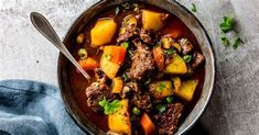 a bowl filled with stew and vegetables on top of a blue cloth next to a spoon