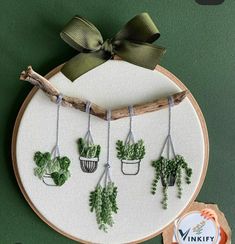 a cross stitch pattern with plants hanging from it's sides and a ribbon tied around the hoop