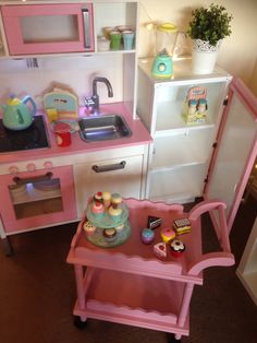 a doll house kitchen with pink furniture and accessories on the table, including a toy oven