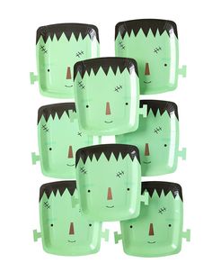 six green plates with faces on them and one has a black head in the middle