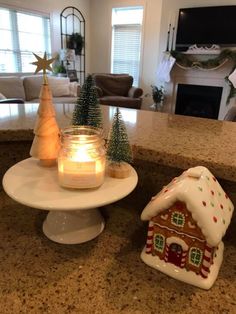 a candle sits on a cake plate next to a gingerbread house and christmas tree