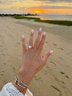 a woman's hand with pink manicures and ring on the beach at sunset