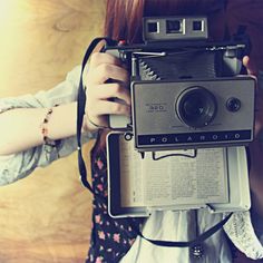 a woman holding an old polaroid camera in front of her face