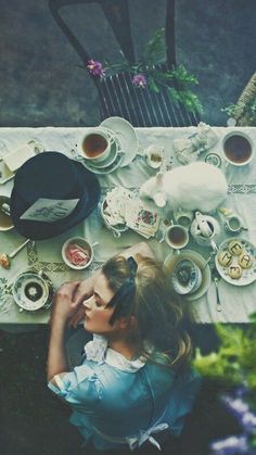 a woman sitting at a table covered in tea cups