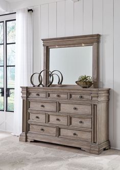 a dresser with a mirror on top of it in front of a white wall and window