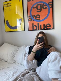 a woman laying in bed taking a selfie with her cell phone and two posters on the wall behind her