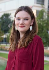 a woman standing in front of a building wearing a red shirt and white hoop earrings