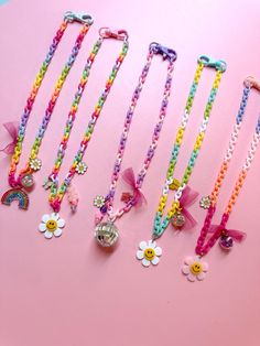 five different colored necklaces on a pink surface with flowers and charms attached to them