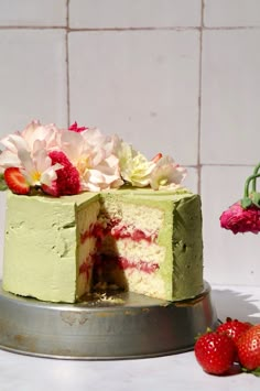 a green cake with flowers and strawberries on the side