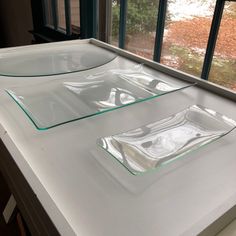 two rectangular glass plates sitting on top of a white counter next to a large window