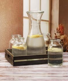 three glass vases sitting on top of a wooden tray with lemon slices in them