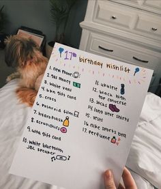 a person holding up a birthday wish list with a dog sitting on the bed behind them