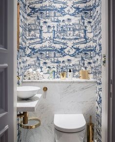 a white toilet sitting next to a sink in a bathroom under a blue and white wall