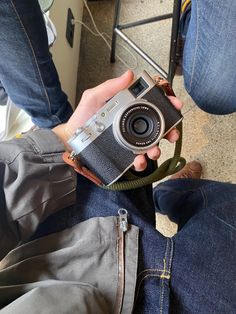 a person holding an old camera in their hand while sitting on the floor next to a chair