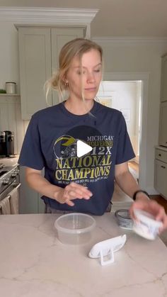 a woman standing in front of a kitchen counter holding a bowl and measuring spoons