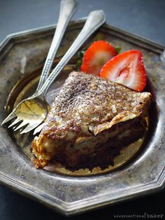 a piece of french toast on a plate with strawberries and silverware next to it