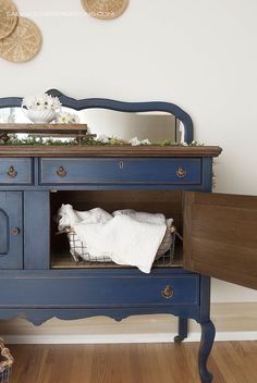 a blue dresser with baskets on top and a mirror above it