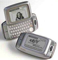 two old cell phones are sitting side by side on a white surface, one has a woman's face on the screen