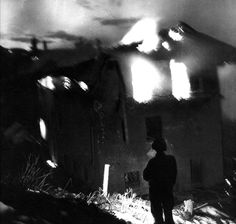 a person standing in front of a house with fire coming out of the roof and windows