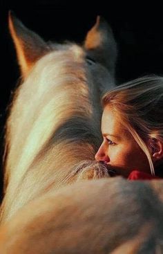 a woman with long blonde hair standing next to a large white horse in the dark