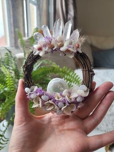 a hand holding a wicker wreath with flowers and an acrylic ball in it