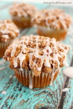 three muffins with icing on top sitting on a blue table next to spoon