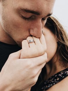 a man and woman kissing each other while holding their hands to their mouth with the ring on his finger