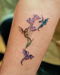 a tattoo on the leg of a woman with purple flowers and two green dragon's